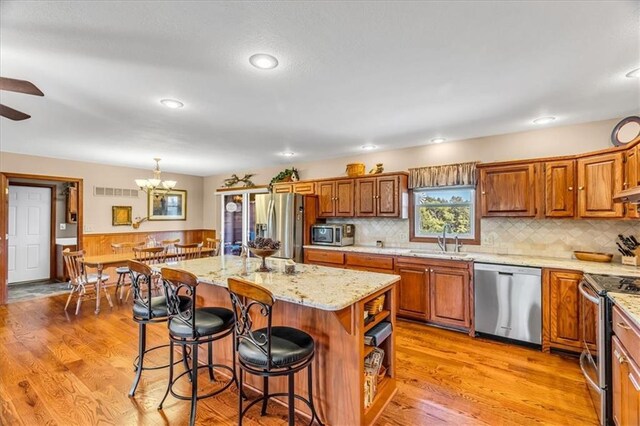 kitchen with decorative light fixtures, a chandelier, appliances with stainless steel finishes, a center island, and light wood-type flooring