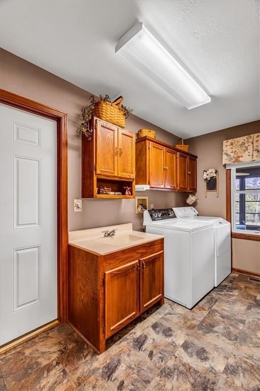 laundry room featuring a textured ceiling, sink, washing machine and clothes dryer, and cabinets