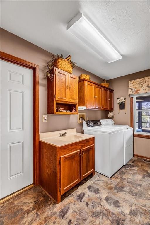 laundry room featuring cabinet space, baseboards, washer and clothes dryer, stone finish flooring, and a sink