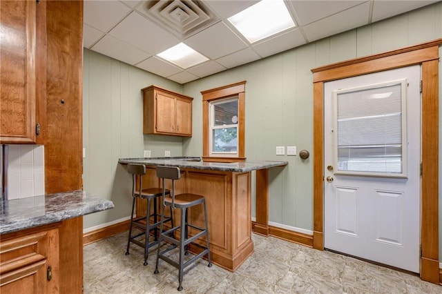 kitchen featuring a paneled ceiling, kitchen peninsula, dark stone countertops, and a breakfast bar area