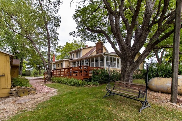 back of property with a wooden deck, a sunroom, and a yard