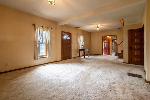 entrance foyer with beamed ceiling, light colored carpet, and a textured ceiling