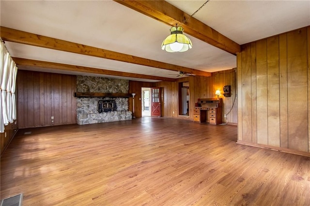 unfurnished living room with ceiling fan, light hardwood / wood-style flooring, beamed ceiling, wooden walls, and a fireplace