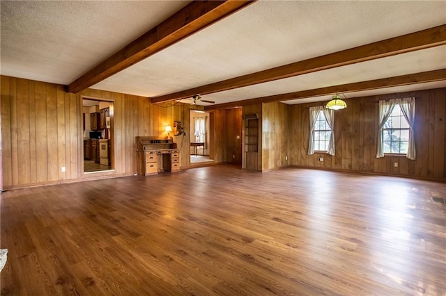 unfurnished living room featuring hardwood / wood-style flooring, beam ceiling, a textured ceiling, and wooden walls