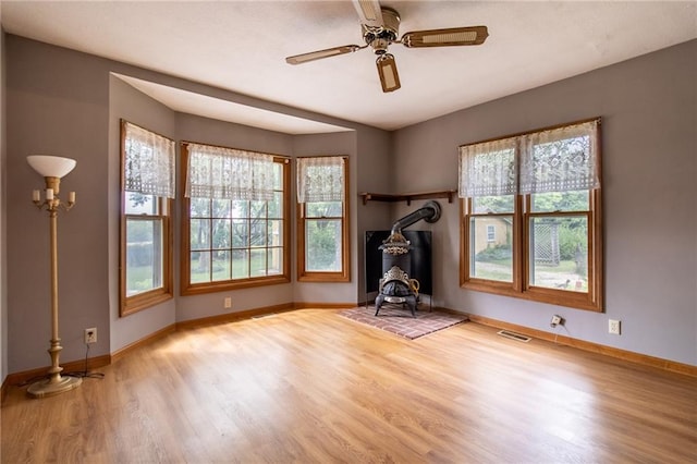 spare room featuring ceiling fan, a wood stove, and light hardwood / wood-style flooring