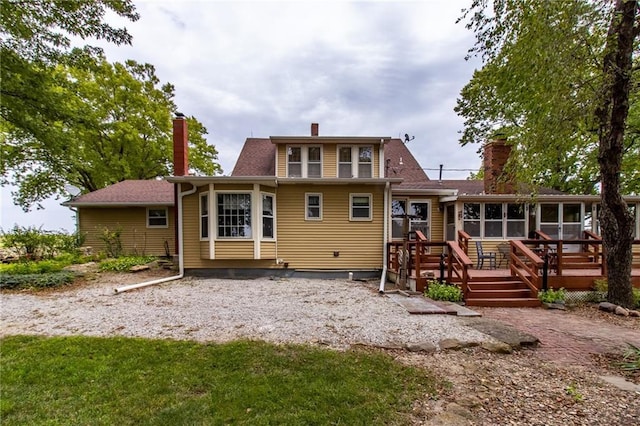 back of property featuring a sunroom, a wooden deck, and a lawn