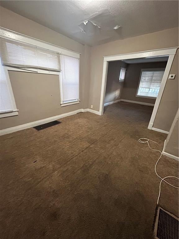 empty room with baseboards, dark colored carpet, and a textured ceiling