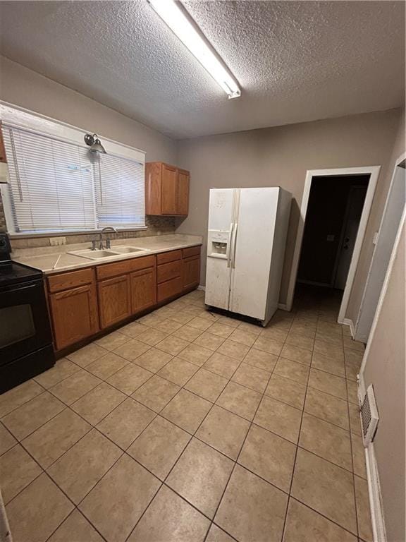 kitchen featuring white fridge with ice dispenser, black electric range, brown cabinetry, and a sink