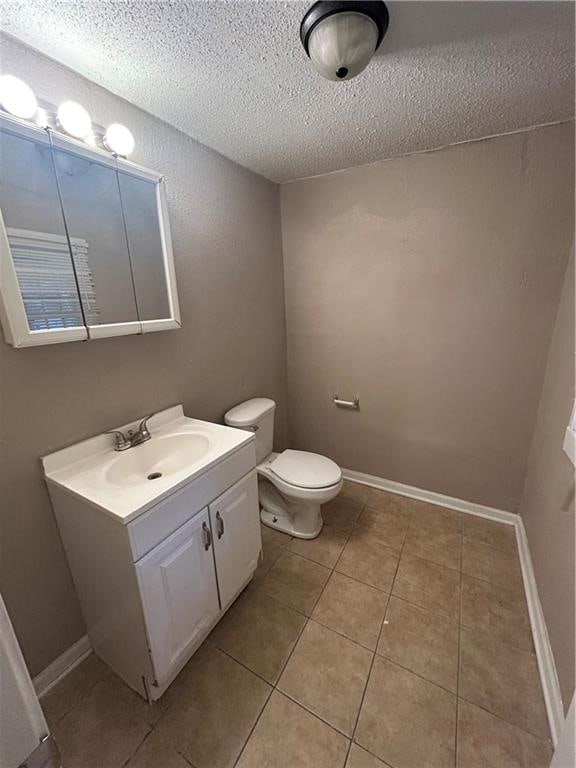 half bathroom with toilet, vanity, a textured ceiling, tile patterned flooring, and baseboards