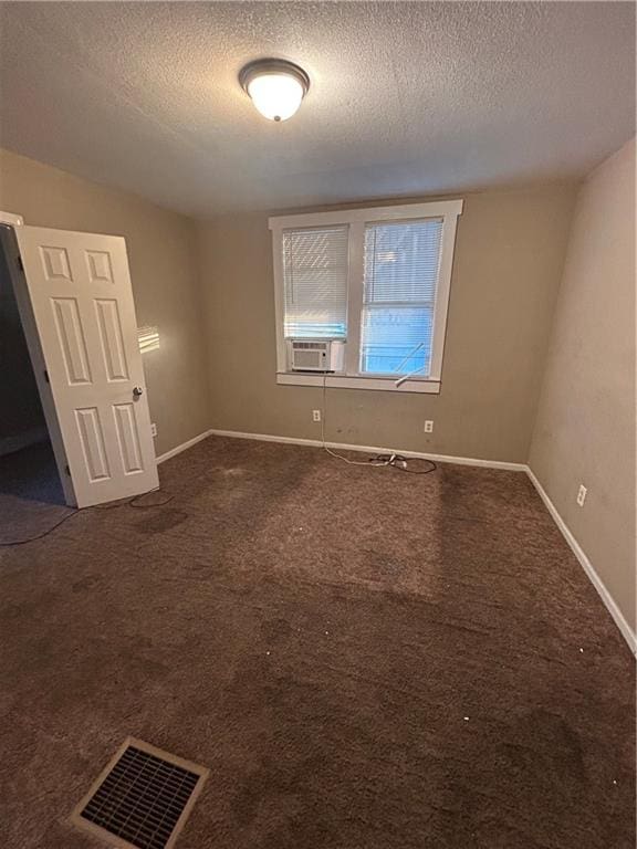 unfurnished bedroom with a textured ceiling, dark colored carpet, visible vents, and baseboards