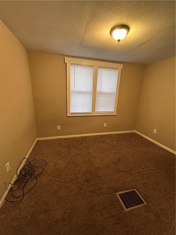 spare room with a textured ceiling, dark colored carpet, visible vents, and baseboards