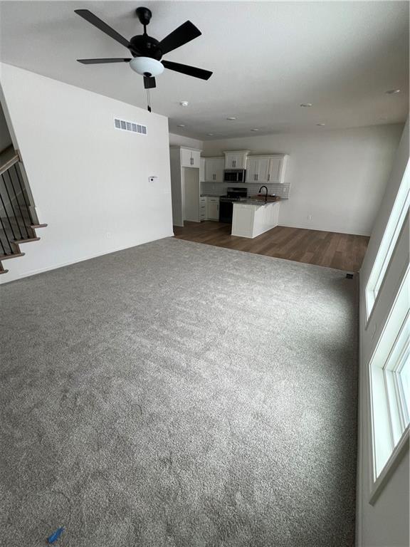 unfurnished living room with ceiling fan, dark carpet, and sink