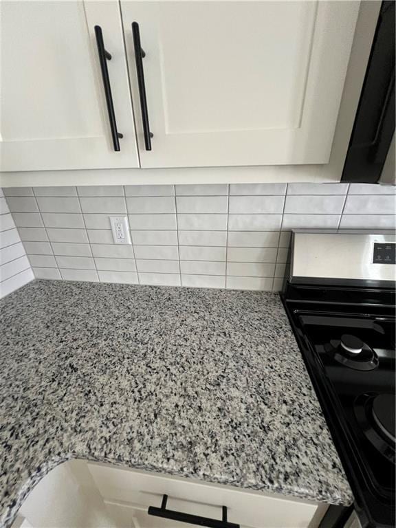 interior details featuring backsplash, black electric range oven, light stone countertops, and white cabinets