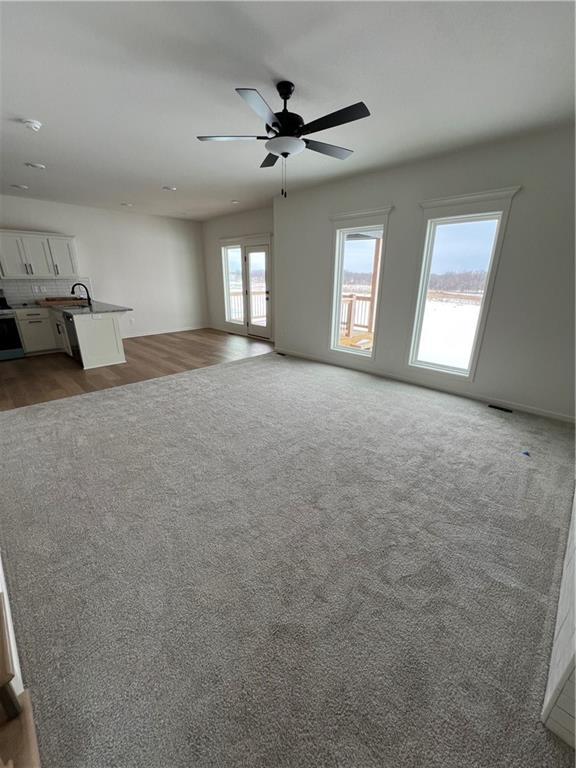 unfurnished living room with ceiling fan, sink, carpet floors, and french doors