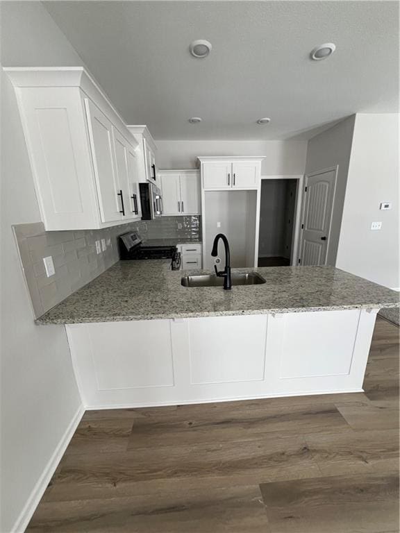 kitchen with light stone countertops, kitchen peninsula, stainless steel appliances, sink, and white cabinets