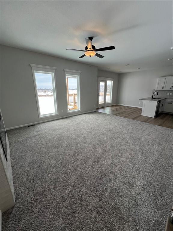 unfurnished living room featuring ceiling fan, sink, and dark carpet