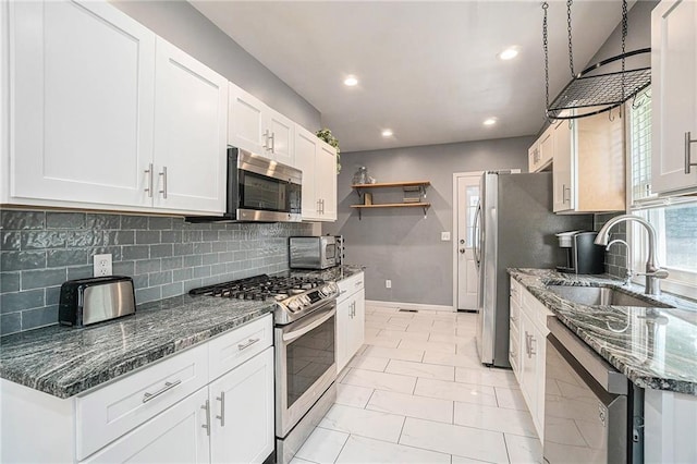 kitchen with a sink, stainless steel appliances, white cabinets, and dark stone counters