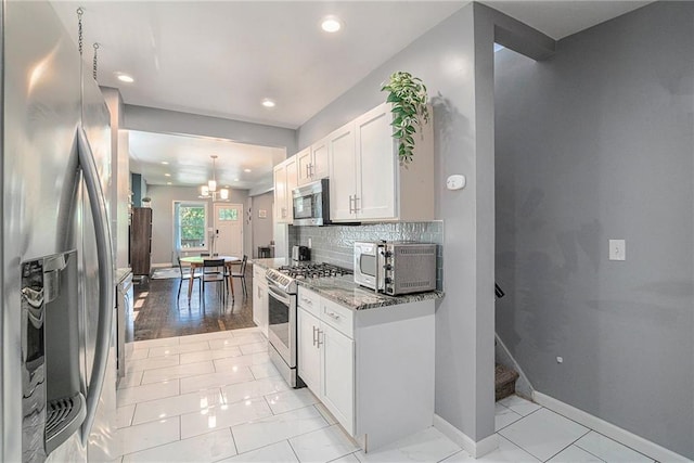 kitchen with backsplash, white cabinetry, stainless steel appliances, baseboards, and light stone countertops