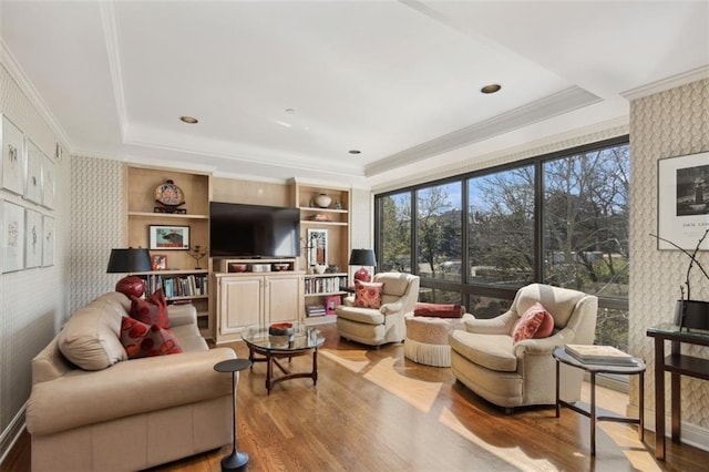 living room with light hardwood / wood-style flooring, a tray ceiling, ornamental molding, and built in features