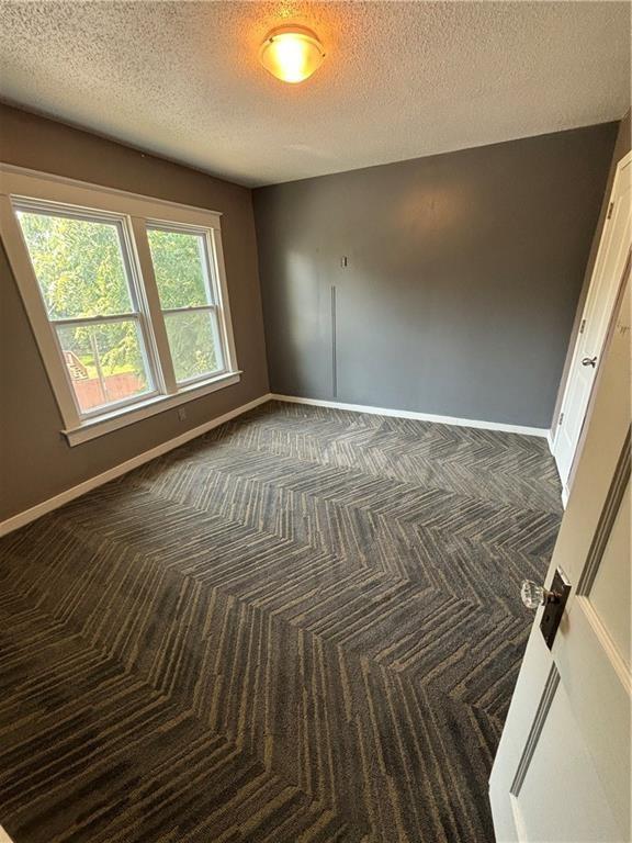 empty room with a textured ceiling and dark carpet