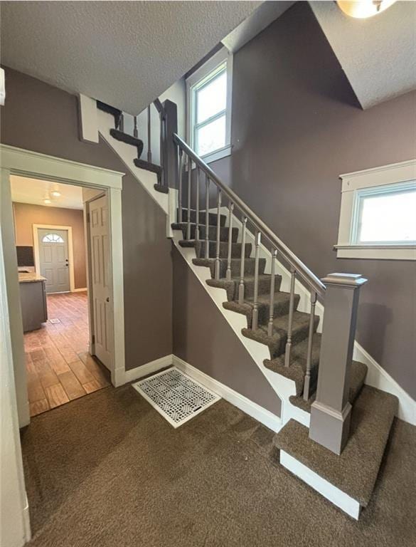 stairway featuring a textured ceiling, carpet flooring, and a healthy amount of sunlight