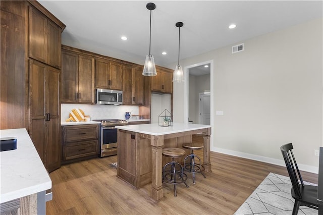 kitchen featuring a center island, hanging light fixtures, stainless steel appliances, tasteful backsplash, and light hardwood / wood-style flooring