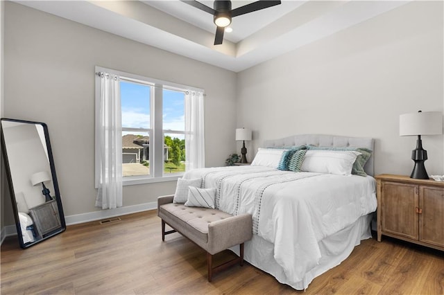 bedroom featuring ceiling fan, light hardwood / wood-style floors, and a raised ceiling