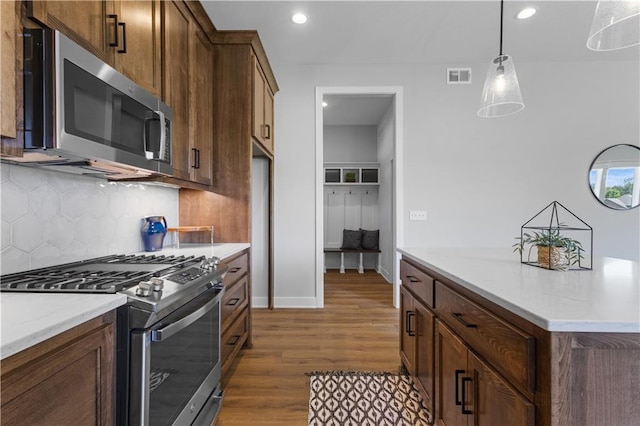 kitchen with light stone countertops, dark wood-type flooring, decorative light fixtures, decorative backsplash, and appliances with stainless steel finishes