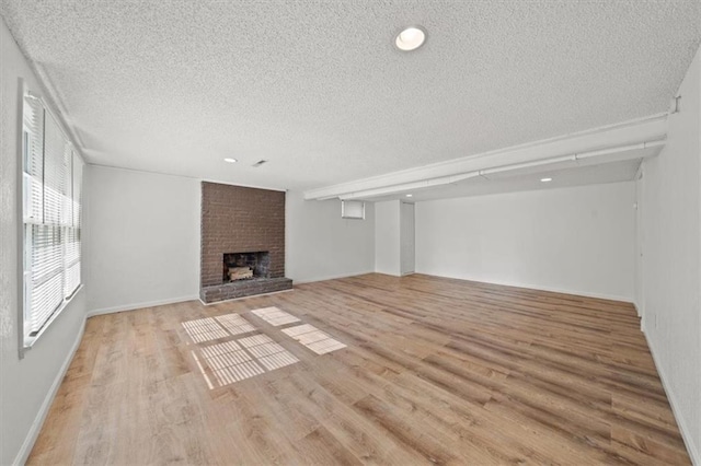 unfurnished living room with a textured ceiling, a brick fireplace, light hardwood / wood-style flooring, and brick wall