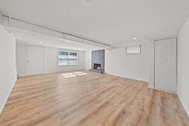 basement featuring light hardwood / wood-style flooring, a textured ceiling, brick wall, and a fireplace