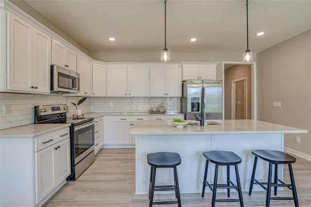 kitchen with appliances with stainless steel finishes, a center island with sink, light wood-type flooring, and tasteful backsplash