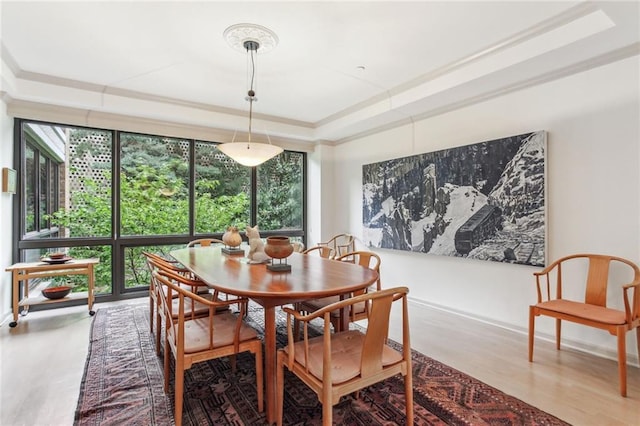 dining room featuring a tray ceiling, baseboards, wood finished floors, and ornamental molding