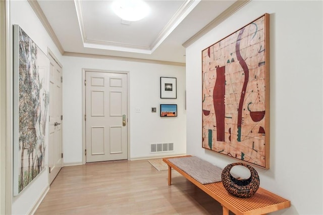 foyer featuring light wood-type flooring, a tray ceiling, visible vents, and ornamental molding