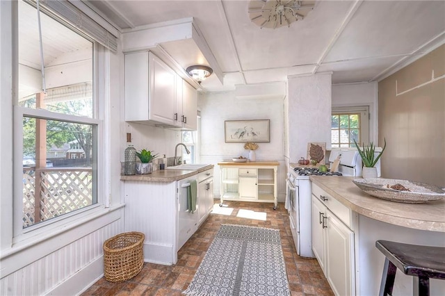 kitchen with white gas range oven, white cabinetry, stainless steel dishwasher, and sink