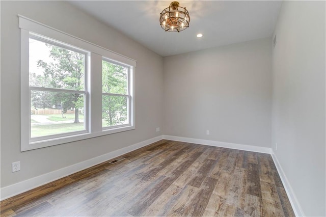 empty room featuring wood-type flooring, a wealth of natural light, and a chandelier