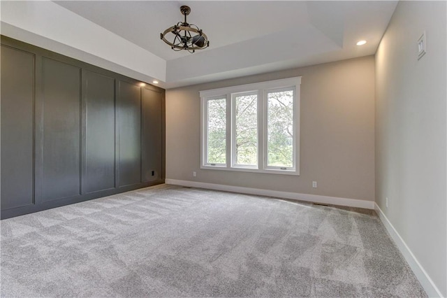 carpeted empty room featuring a raised ceiling and a notable chandelier