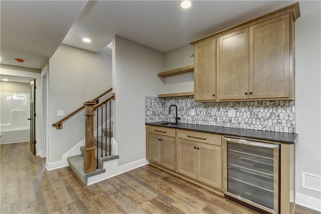 bar with beverage cooler, sink, tasteful backsplash, and light hardwood / wood-style floors