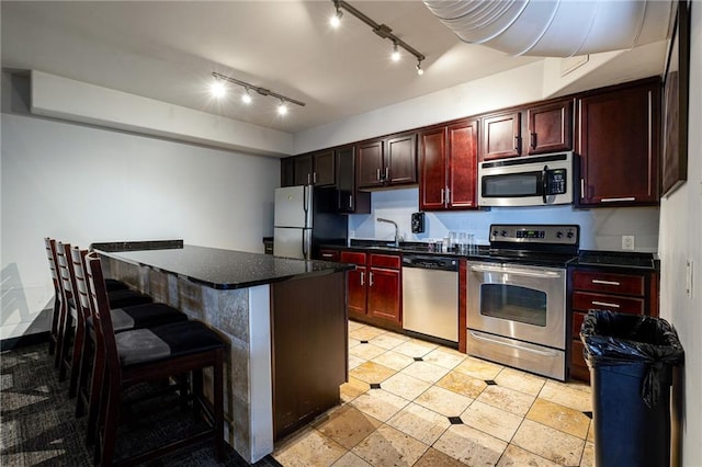 kitchen with track lighting, a kitchen breakfast bar, a kitchen island, and stainless steel appliances