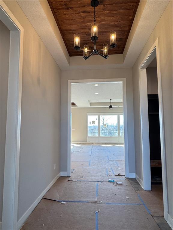 corridor with a notable chandelier, wooden ceiling, and a tray ceiling