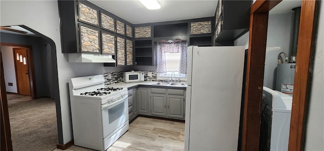 kitchen featuring under cabinet range hood, white appliances, a sink, light countertops, and washer / clothes dryer