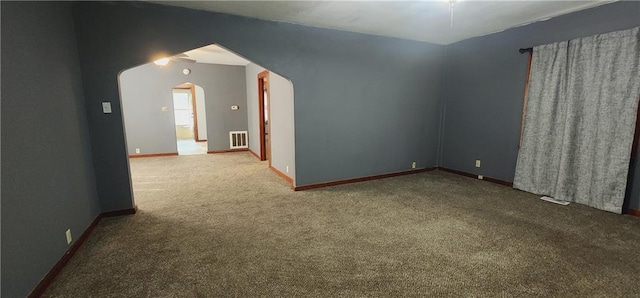 empty room featuring arched walkways, dark carpet, visible vents, and baseboards