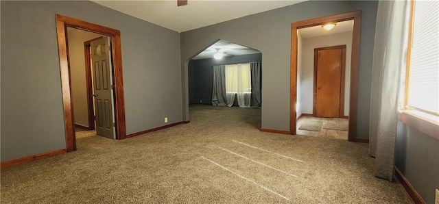 hallway featuring baseboards, arched walkways, and light colored carpet