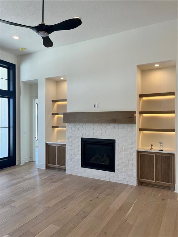 unfurnished living room with hardwood / wood-style floors, built in shelves, ceiling fan, a textured ceiling, and a glass covered fireplace