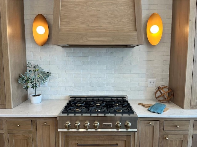 kitchen with brown cabinetry, light stone countertops, backsplash, and stainless steel gas cooktop