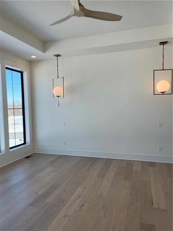 empty room featuring ceiling fan, visible vents, baseboards, and wood finished floors