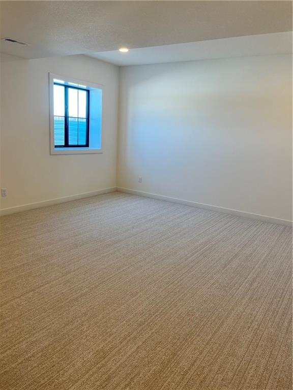 empty room with a textured ceiling, visible vents, baseboards, vaulted ceiling, and light carpet