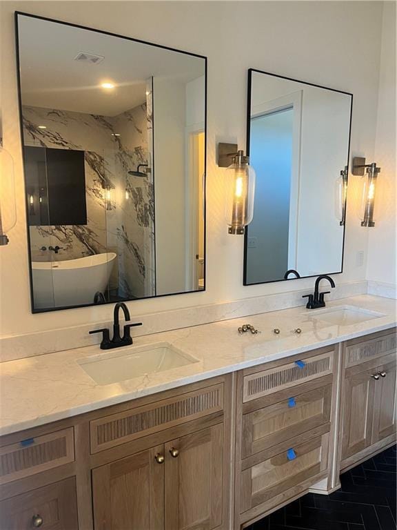 full bath with a sink, a marble finish shower, and double vanity