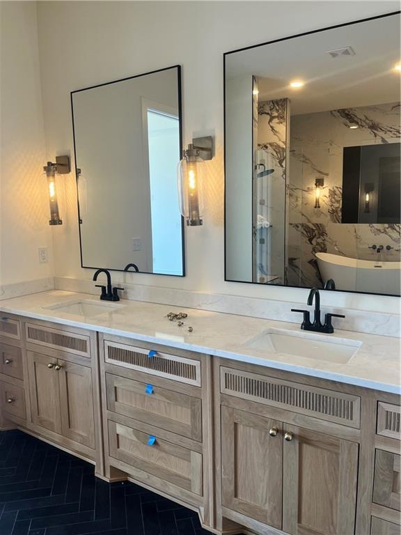 full bath featuring double vanity, visible vents, a marble finish shower, and a sink