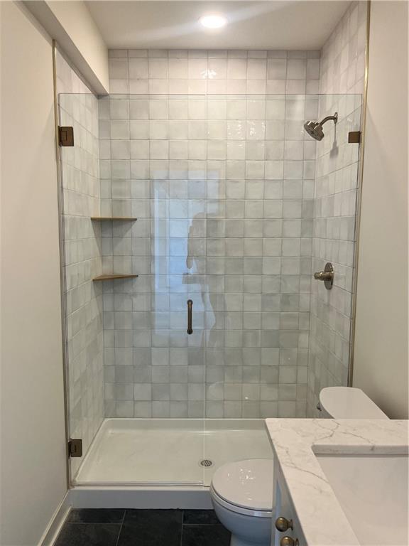 bathroom featuring tile patterned flooring, a shower stall, toilet, and vanity