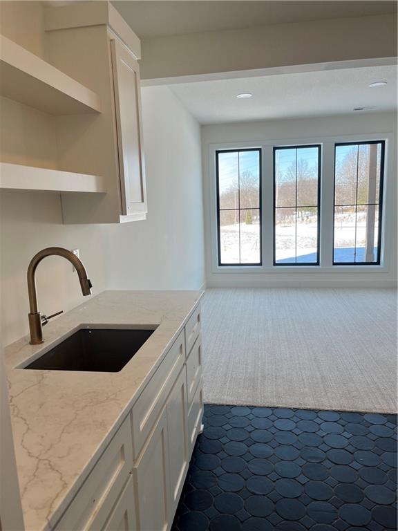 kitchen featuring a sink, light stone counters, white cabinets, dark colored carpet, and open shelves